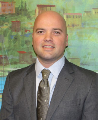 A bald man in a business suit and tie stands smiling in front of a colorful, abstract landscape. This portrait exemplifies professionalism and approachability.