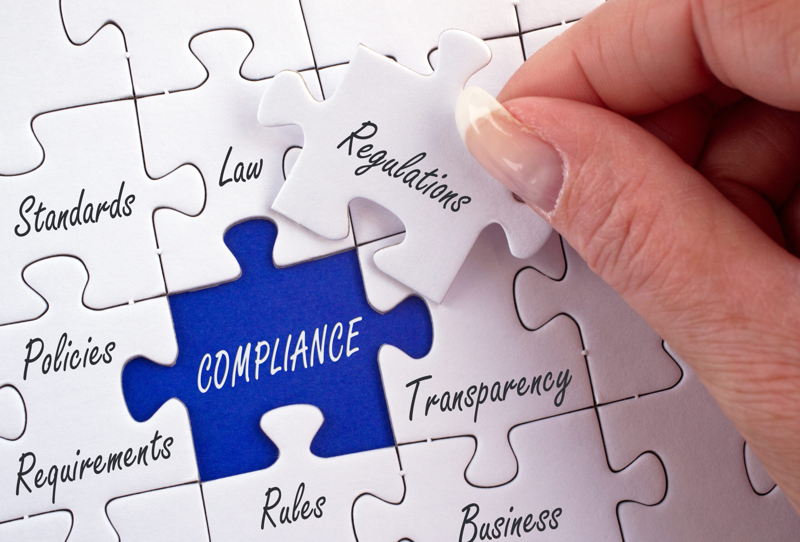 Hand placing a puzzle piece labeled "Regulations" into a larger puzzle with "Compliance" highlighted in blue, symbolizing the importance of regulatory adherence.